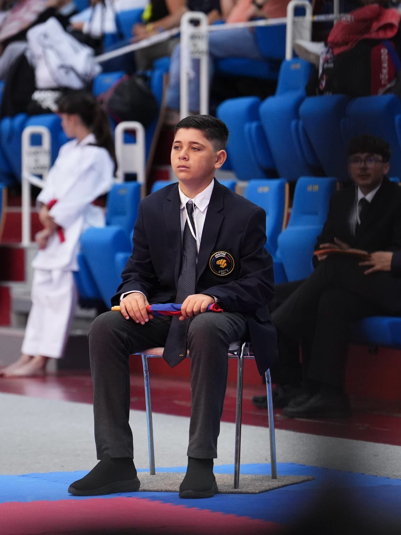 Jeune arbitre KTE assis au bord du tatami avec les drapeaux rouge et bleu